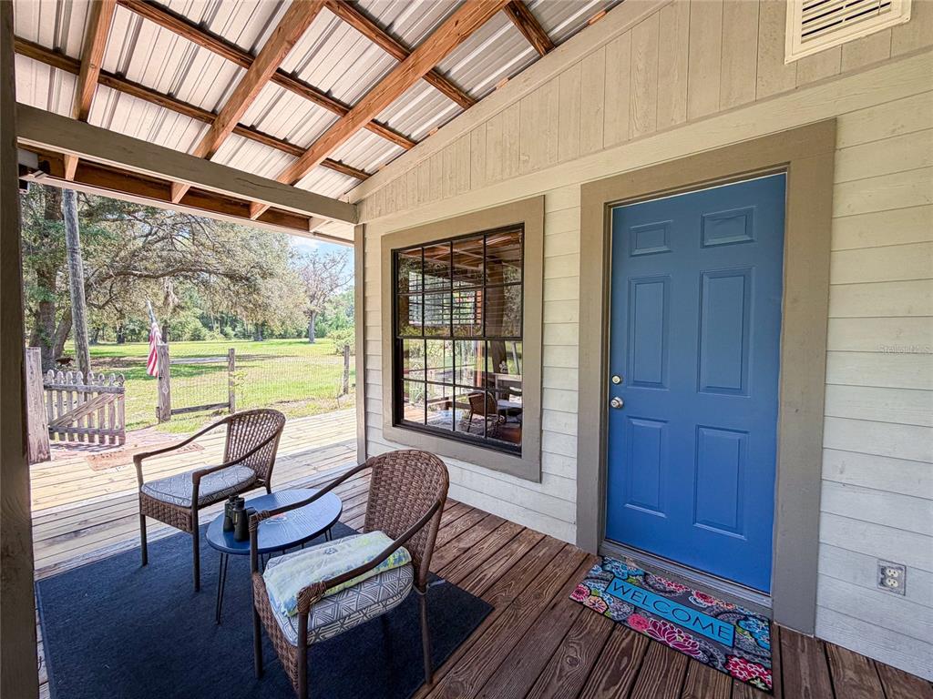 A covered wooden porch features two wicker chairs, a small table, and a blue front door — 28622 N STATE ROAD 121, ALACHUA, FL