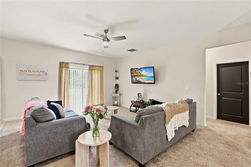 A living room features two gray sofas, a wall-mounted television, and beige carpeting — 5724 BANNOCK CIRCLE, NORTH PORT, FL