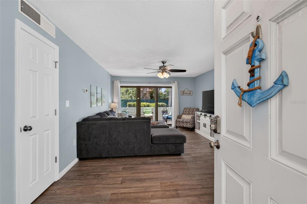 A living room features a dark gray sectional sofa, wood-look flooring, and a sliding glass door — 6300 A1A S UNIT A44D, ST AUGUSTINE, FL