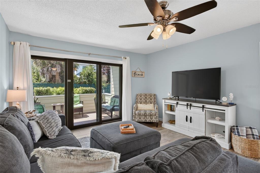 A living room features a grey sectional sofa, a television on a white console, and sliding doors — 6300 A1A S UNIT A44D, ST AUGUSTINE, FL
