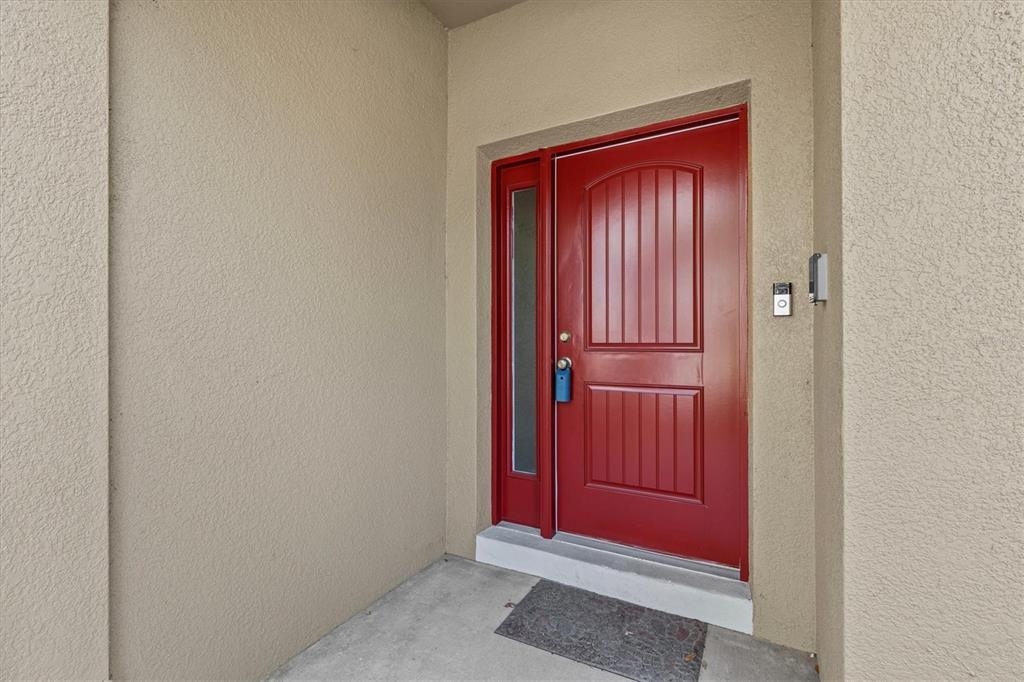 A bright red front door with a side window is set into a beige stucco wall — 800 CALLISTA CAY LOOP, TARPON SPRINGS, FL