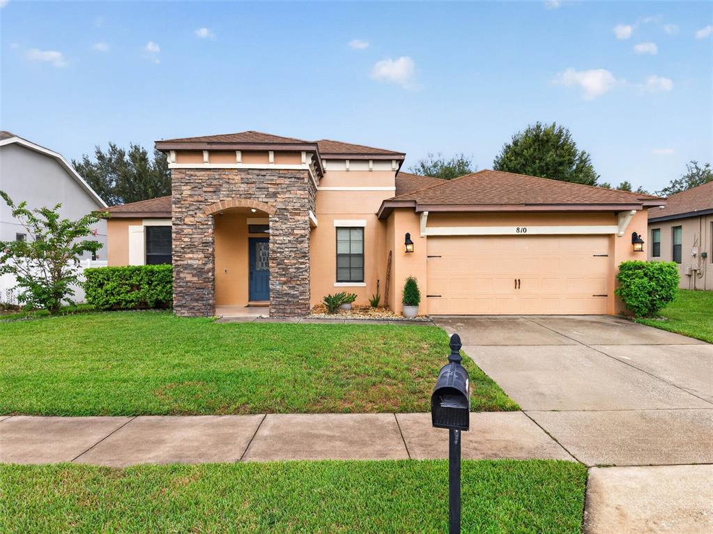 A single-story house features a stone-accented entryway, a two-car garage, and a manicured front lawn — 810 WOODS LANDING DRIVE, MINNEOLA, FL