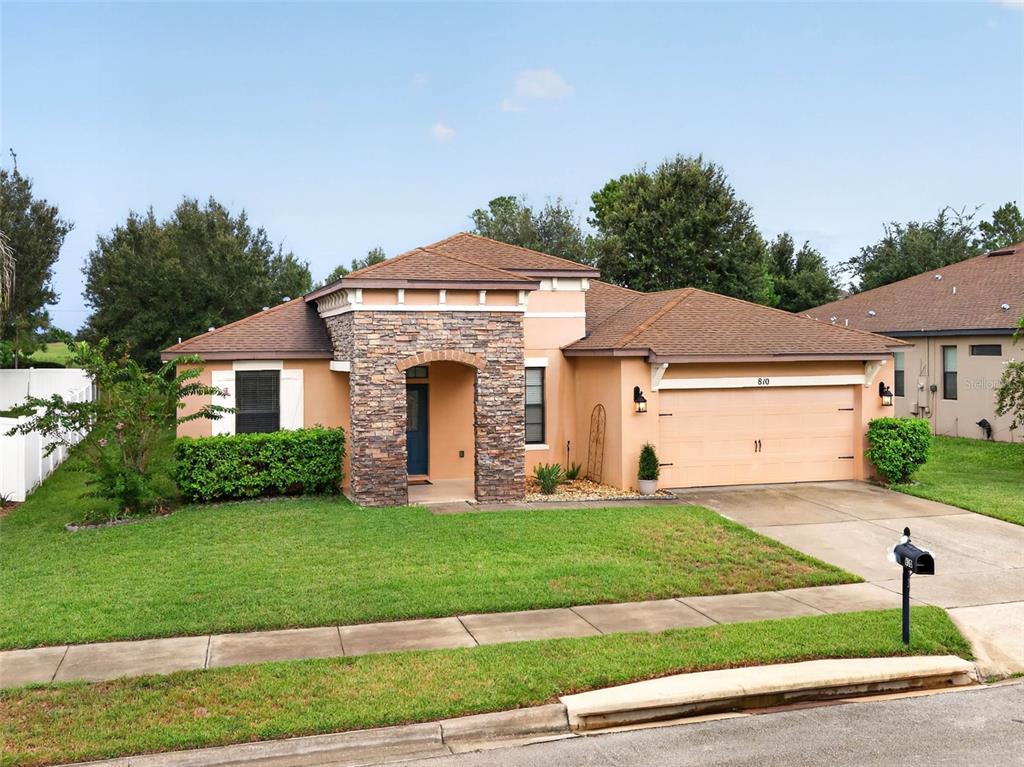 A single-story house with a stone-accented entryway, tan stucco walls, and a two-car garage — 810 WOODS LANDING DRIVE, MINNEOLA, FL