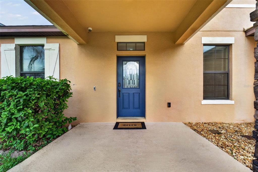 A blue front door with a glass insert is centered under a covered entryway — 810 WOODS LANDING DRIVE, MINNEOLA, FL