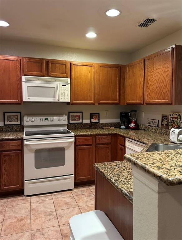 A kitchen features wood cabinets, granite countertops, white appliances, and tiled flooring — 4600 E MOODY BOULEVARD UNIT 3J, BUNNELL, FL