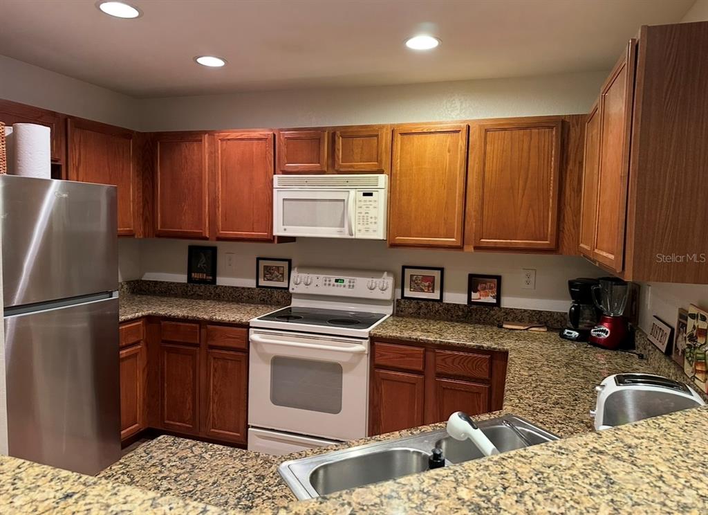 A kitchen features wood cabinets, granite countertops, a stainless steel refrigerator, and white appliances — 4600 E MOODY BOULEVARD UNIT 3J, BUNNELL, FL