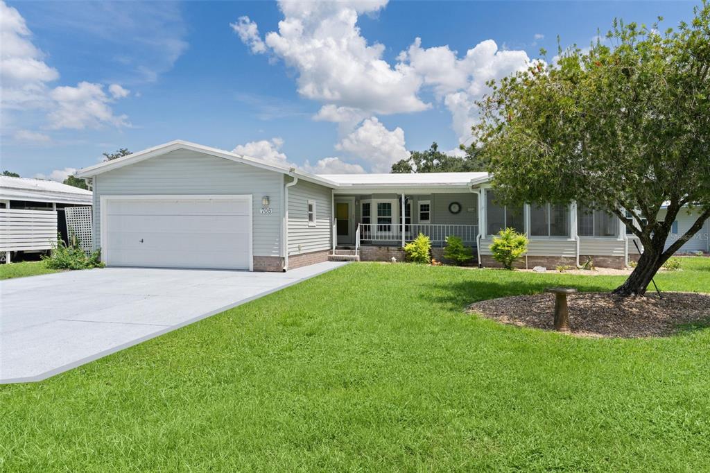 A single-story house with light siding, a white garage door, and a large front yard — 705 OAK BOULEVARD, WILDWOOD, FL