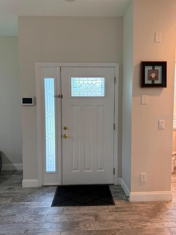 A white front door with a sidelight and glass insert sits in a neutral-toned entryway — 13121 SUMMERTON DRIVE, ORLANDO, FL