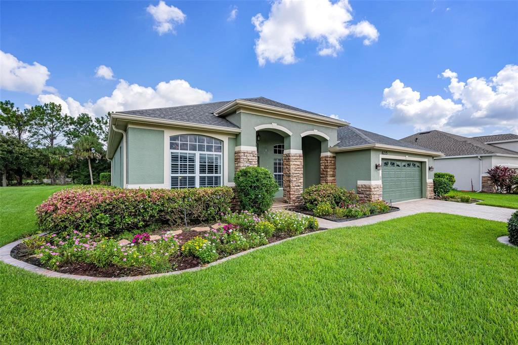 A single-story house with green stucco, stone accents, a two-car garage, and landscaped front yard — 6215 90TH AVENUE CIRCLE E, PARRISH, FL