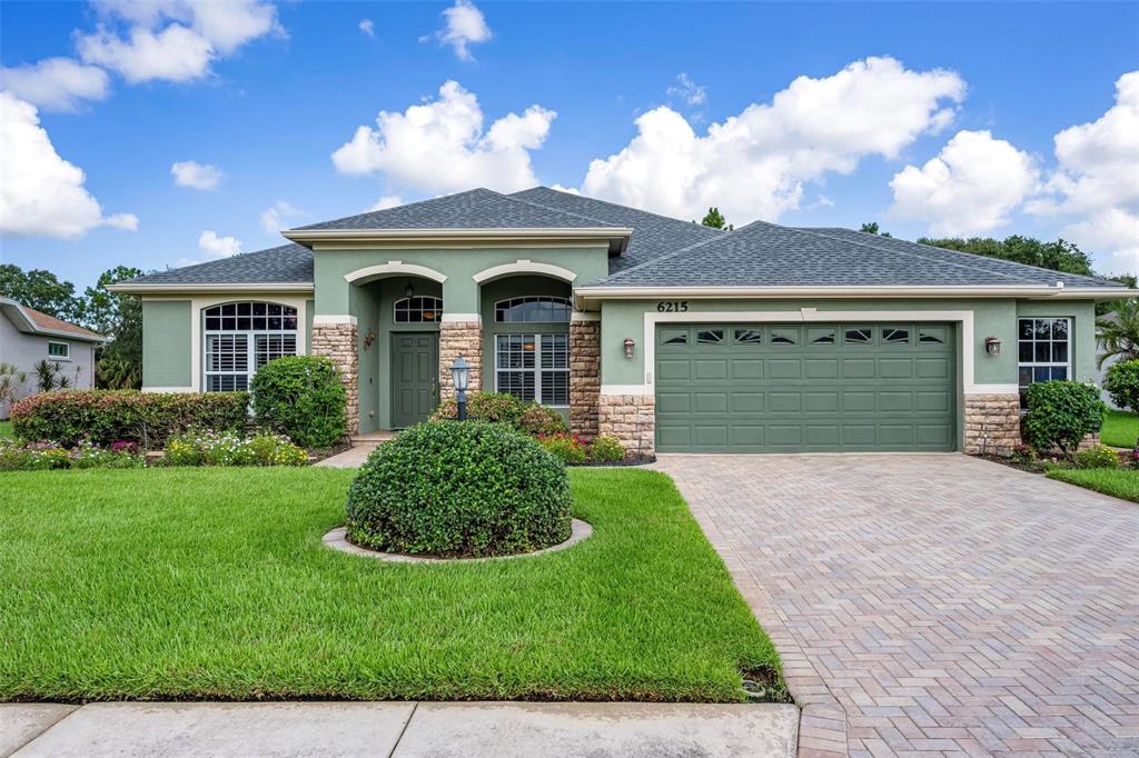 A single-story house with green stucco walls, stone accents, and a paved driveway — 6215 90TH AVENUE CIRCLE E, PARRISH, FL