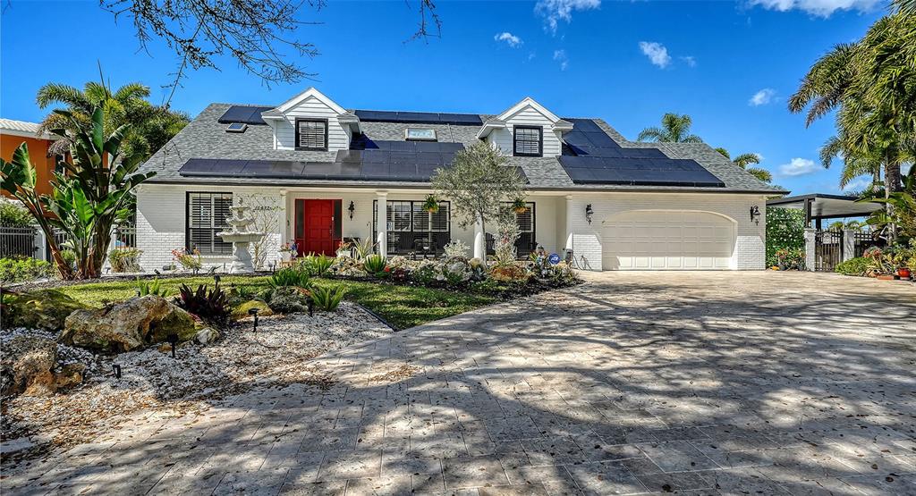 A white brick house with a red door, solar panels, and a paved driveway — 10432 SPOONBILL ROAD W, BRADENTON, FL