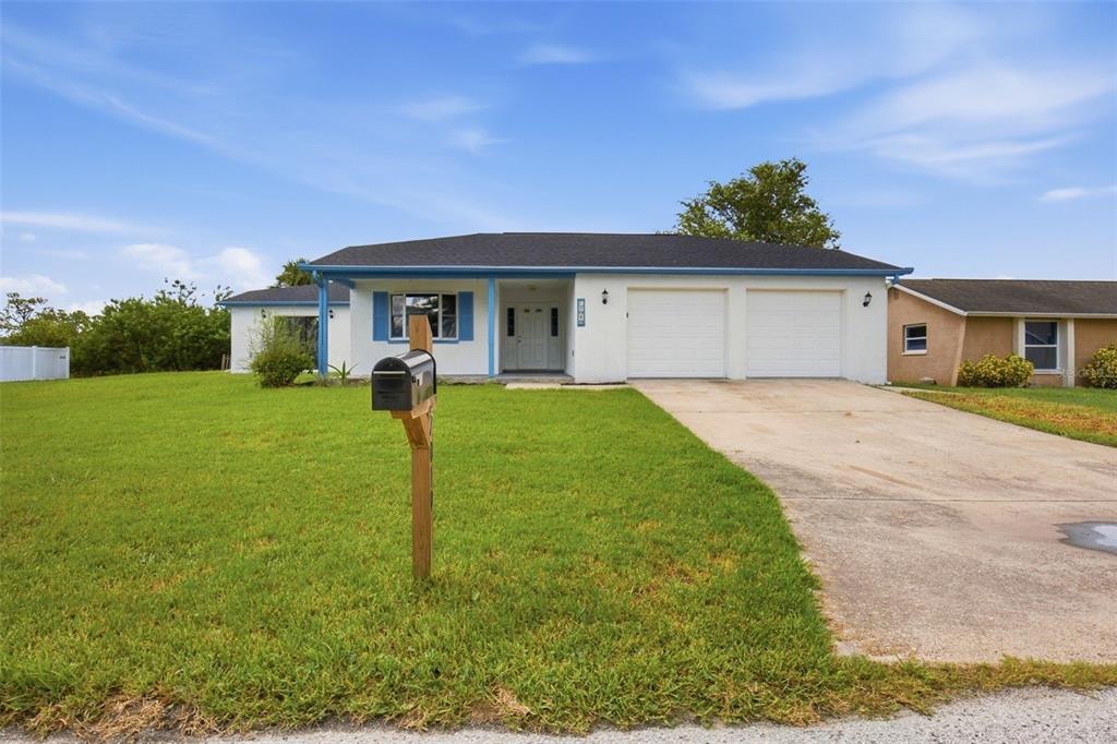 A single-story white house with blue trim, a two-car garage, and a large front lawn — 7010 SOUTHWIND DRIVE, HUDSON, FL