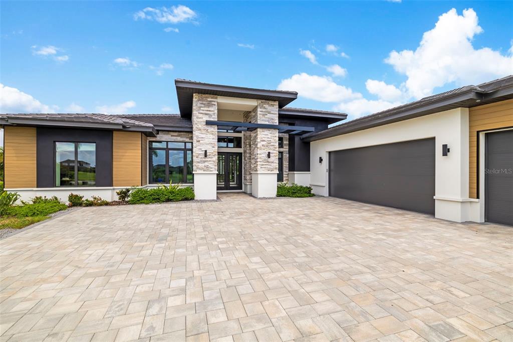 A modern house exterior features a stone entryway, dark garage door, and paved driveway — 4116 BUTTE TRAIL, BRADENTON, FL