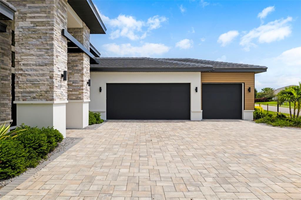 A modern house exterior features a stone pillar, a paved driveway, and two dark garage doors — 4116 BUTTE TRAIL, BRADENTON, FL