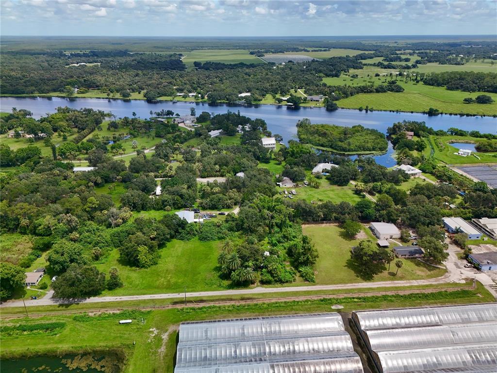 An aerial view shows a river flowing past wooded residential lots and large agricultural greenhouses — 20101 WAGNER AVENUE, ALVA, FL