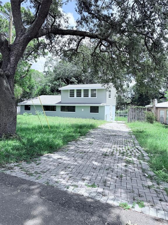 A two-story house with light-colored siding features a paved driveway and large overhanging trees — 10801 N EDISON AVENUE, TAMPA, FL