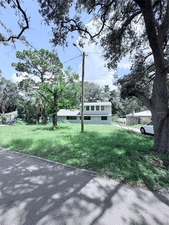 A two-story house with light-colored siding sits behind a large, grassy yard and utility pole — 10801 N EDISON AVENUE, TAMPA, FL