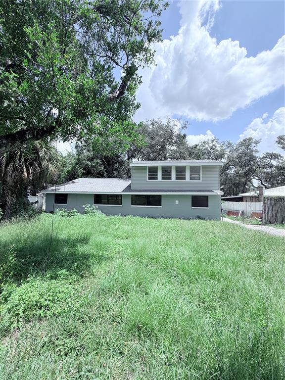 A two-story house with light gray siding sits behind a large, overgrown grassy yard — 10801 N EDISON AVENUE, TAMPA, FL