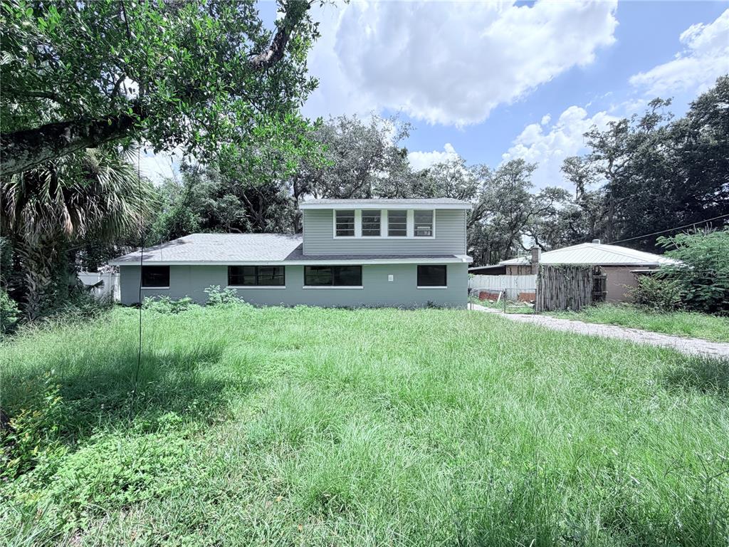 A two-story house with gray siding stands behind a large, overgrown grassy yard — 10801 N EDISON AVENUE, TAMPA, FL
