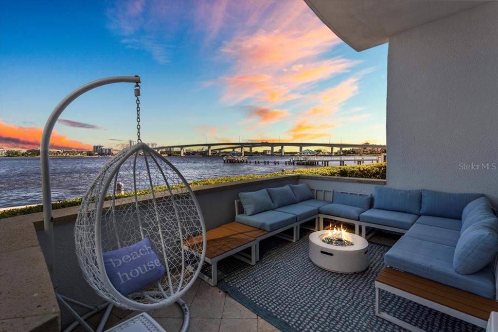 A patio features a hanging chair, sectional seating, and a fire pit overlooking a bridge — 231 RIVERSIDE DRIVE UNIT 102, HOLLY HILL, FL