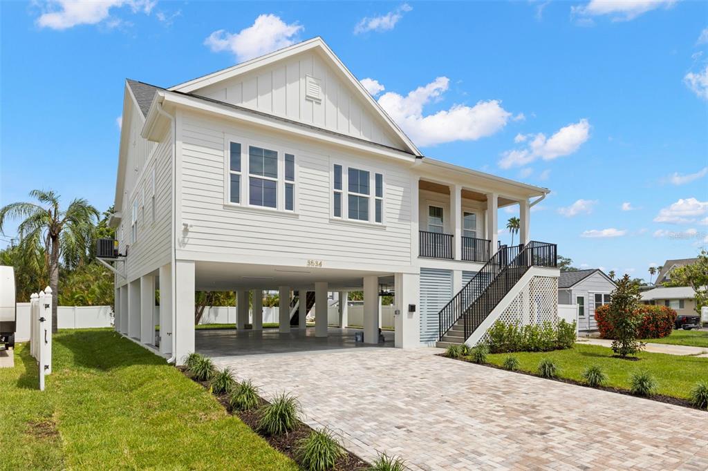 A white elevated house with a paved driveway and a staircase leading to the porch — 3534 OVERLOOK DRIVE NE, ST PETERSBURG, FL