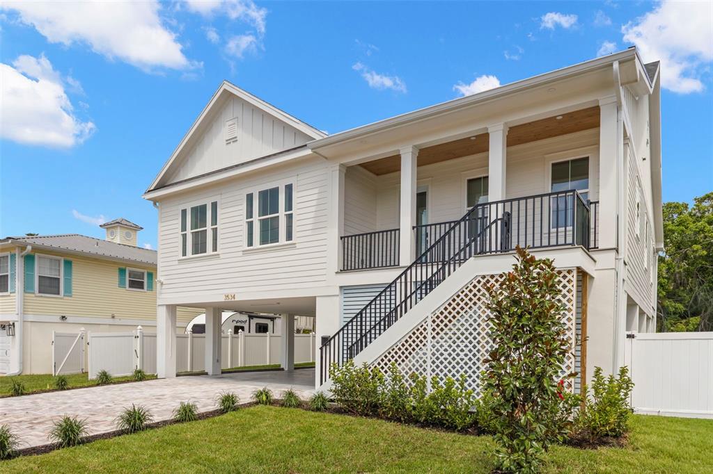 A white elevated house with a front porch, staircase, and paved driveway under the structure — 3534 OVERLOOK DRIVE NE, ST PETERSBURG, FL