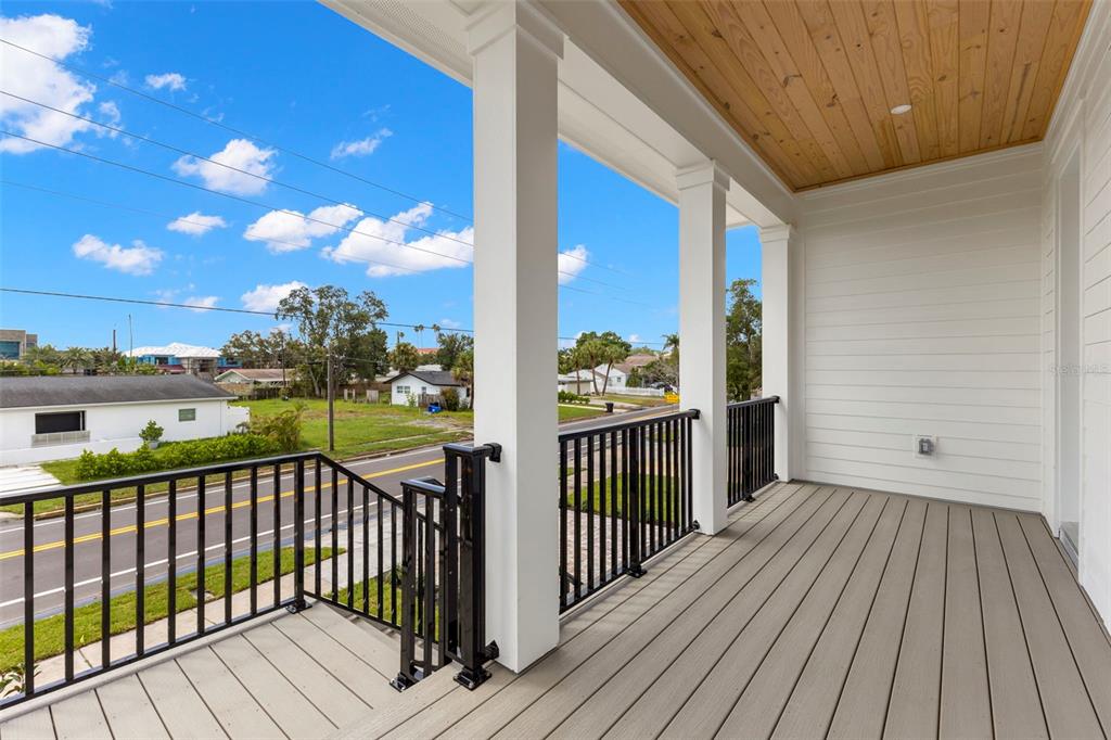 A covered balcony with gray composite decking, white columns, and black metal railings overlooks a street — 3534 OVERLOOK DRIVE NE, ST PETERSBURG, FL