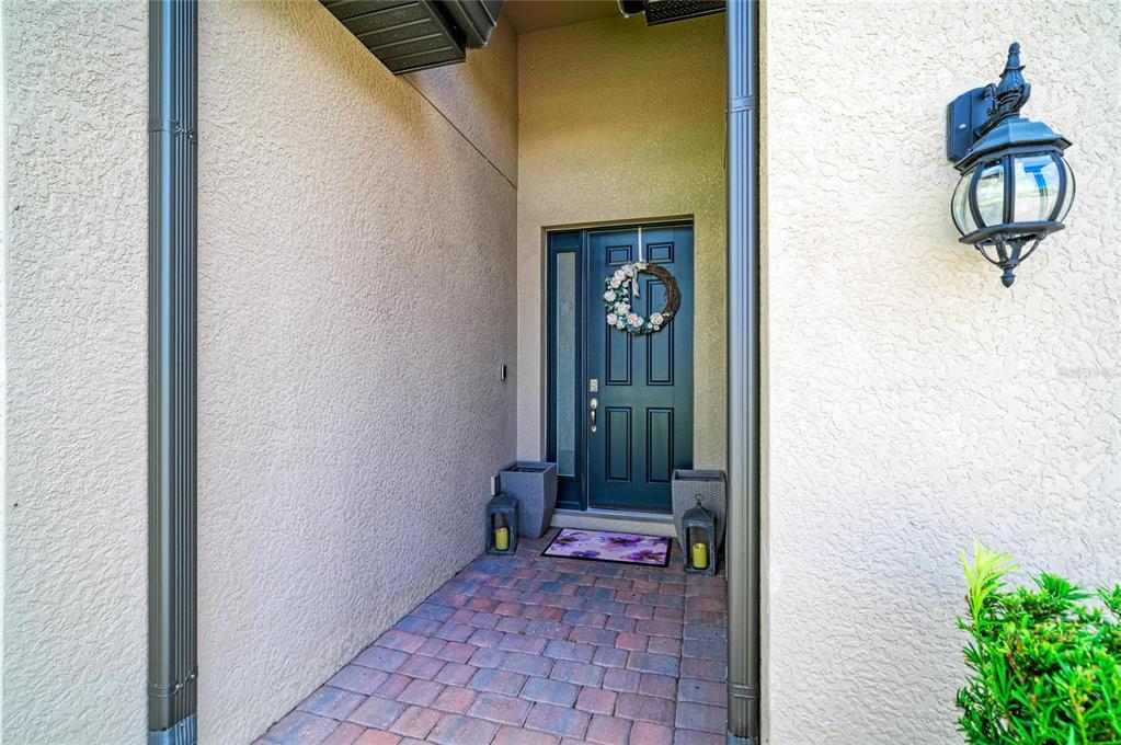 A front entryway features a dark door with a wreath, brick flooring, and wall sconces — 174 VERAZA COURT, NOKOMIS, FL