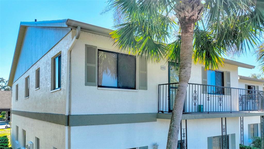 A two-story building exterior features a white stucco facade, a metal balcony railing, and shutters — 6502 RIVER RUN BOULEVARD, WEEKI WACHEE, FL