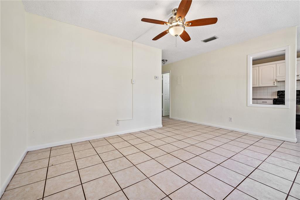 An empty room with beige tile flooring, a ceiling fan, and a kitchen pass-through window — 5225 PEACH AVENUE, SEFFNER, FL
