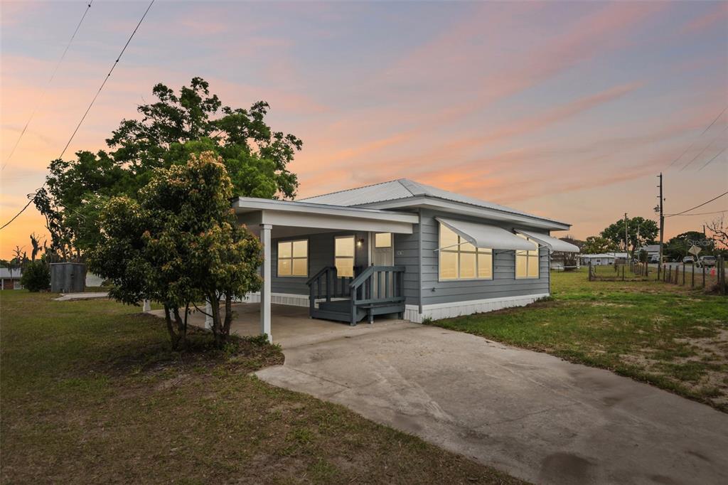 A gray single-story house with a metal roof and a covered carport at sunset — 3070 E CENTRAL AVENUE, BARTOW, FL