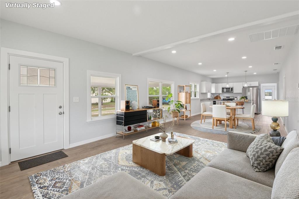 A virtually staged open-concept living and dining area with light wood floors and white walls — 3070 E CENTRAL AVENUE, BARTOW, FL