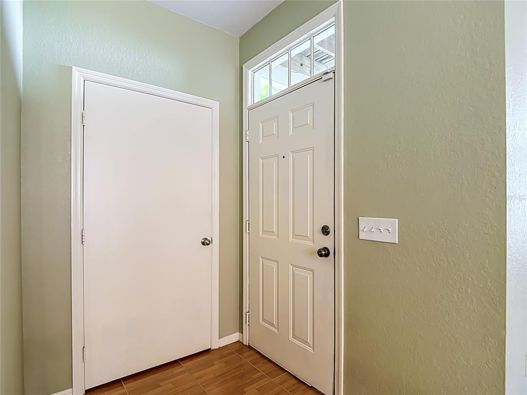 A gray Adirondack chair sits on a tiled porch in front of a dark front door — 4008 BANGALOW PALM COURT, TAMPA, FL