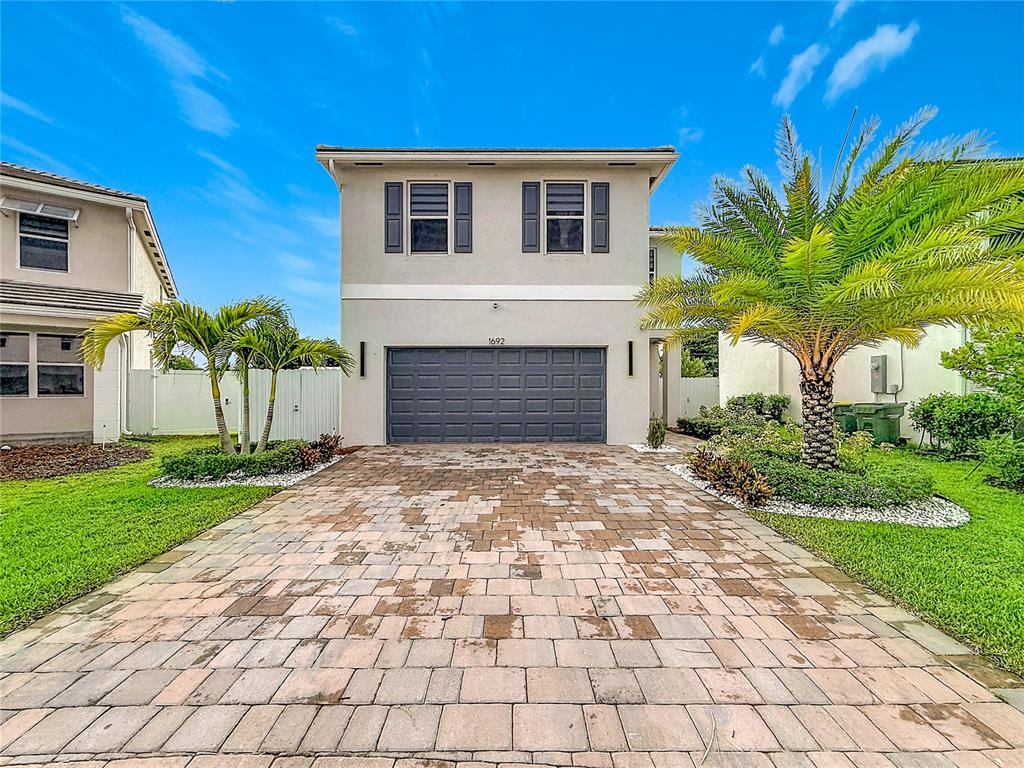 A two-story house with a gray garage, paved driveway, and palm trees under a blue sky — 1692 SE 7TH COURT, HOMESTEAD, FL