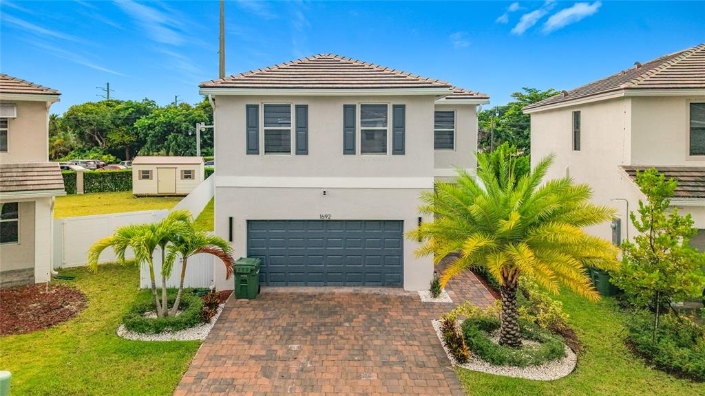 A two-story suburban house with a gray garage, paved driveway, and two palm trees — 1692 SE 7TH COURT, HOMESTEAD, FL