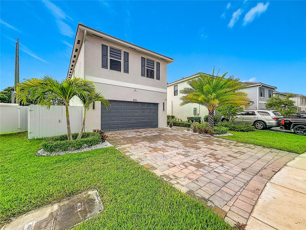 A two-story house with a paved driveway, a two-car garage, and palm trees in front — 1692 SE 7TH COURT, HOMESTEAD, FL