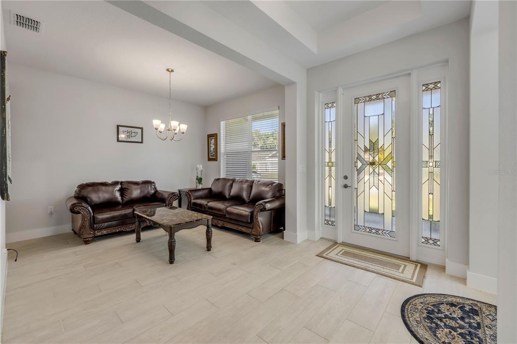 A living room with light tile floors, two brown leather sofas, and a glass-paneled front door — 3034 ADRIAN DRIVE, ORMOND BEACH, FL