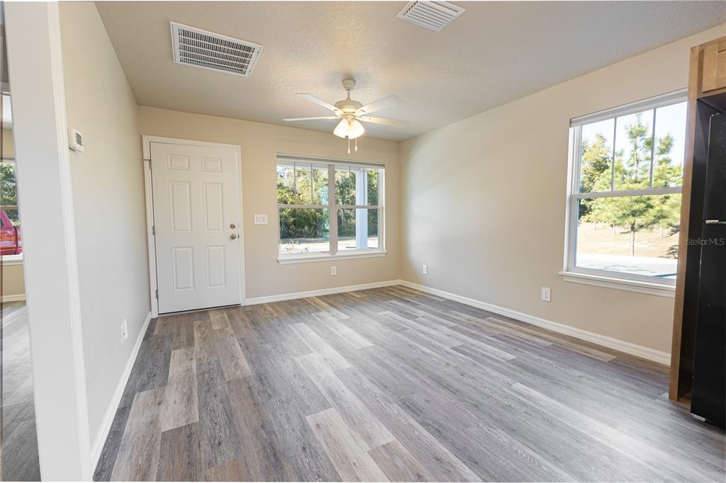 An empty room features light-colored walls, gray wood-look flooring, a ceiling fan, and two windows — 1342 COTTAGE CIRCLE, TAVARES, FL