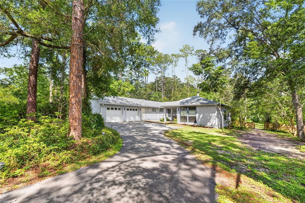 A single-story house with a two-car garage and a paved driveway surrounded by tall trees — 325 NW 80TH BOULEVARD, GAINESVILLE, FL