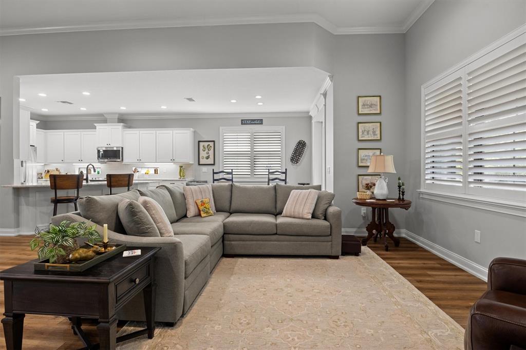 A living room with a grey sectional sofa, wood flooring, and an open kitchen area — 7953 LAKE JAMES BOULEVARD, LAKELAND, FL
