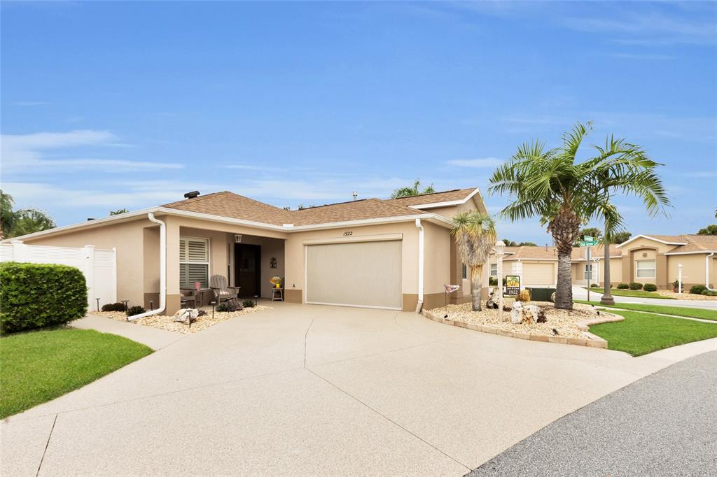 A single-story tan stucco house with a two-car garage and a palm tree in front — 1922 GREELEYVILLE TERRACE, THE VILLAGES, FL
