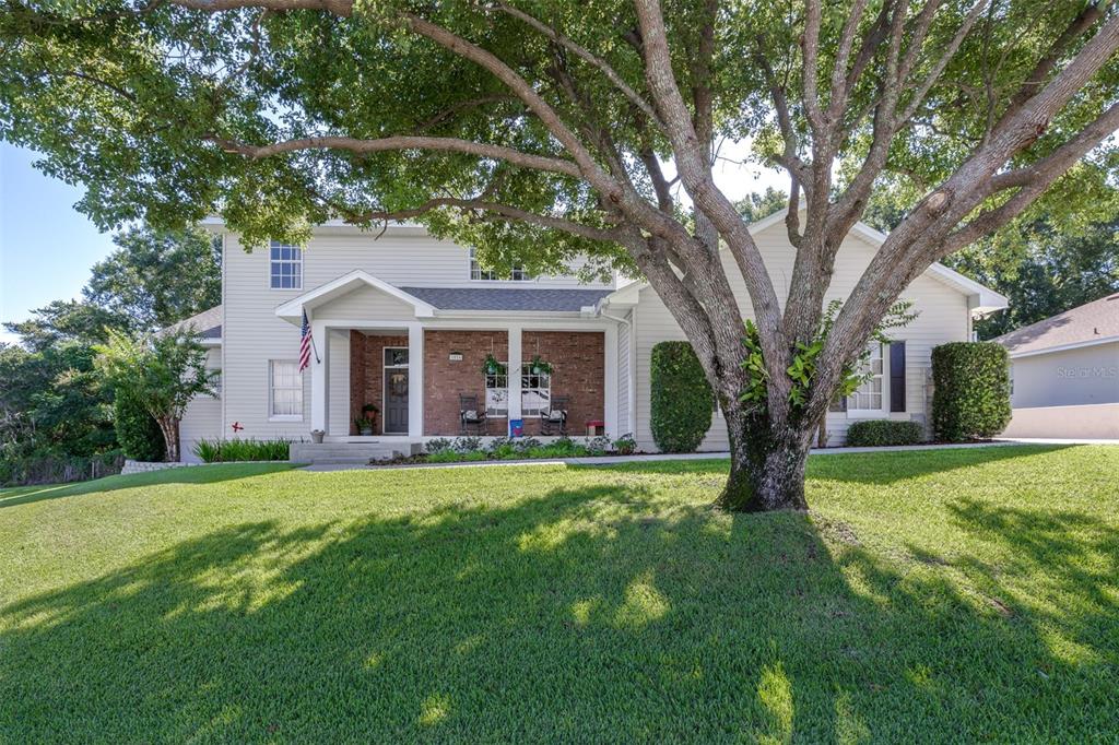 A two-story house with light siding, a brick entryway, and a large tree in front — 1016 S LAKE MARIAM DRIVE, WINTER HAVEN, FL