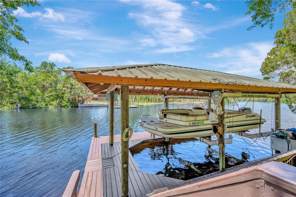A pontoon boat sits on a lift under a covered wooden dock on a river — 11526 RIVER COUNTRY DRIVE, RIVERVIEW, FL