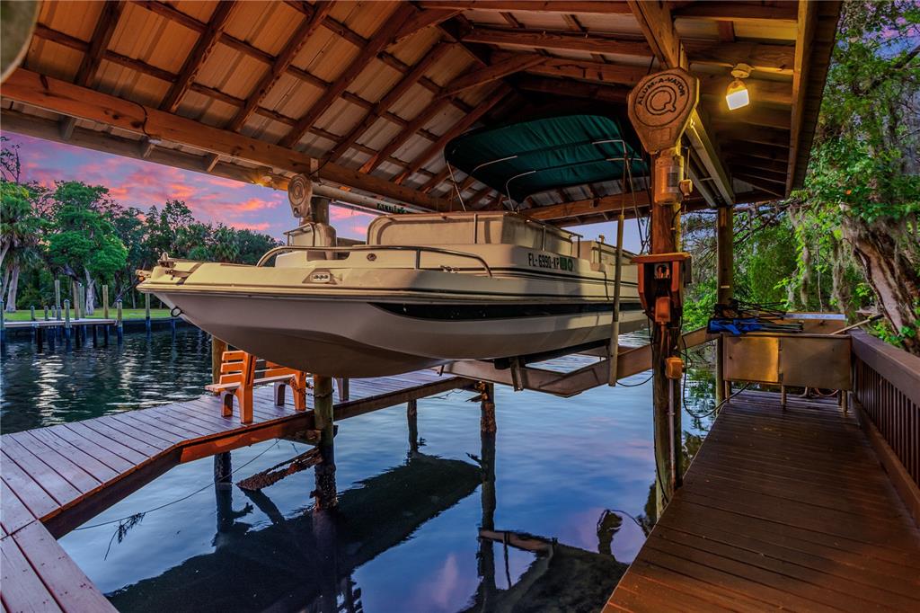 A pontoon boat is suspended on a lift inside a covered wooden boat dock — 11526 RIVER COUNTRY DRIVE, RIVERVIEW, FL