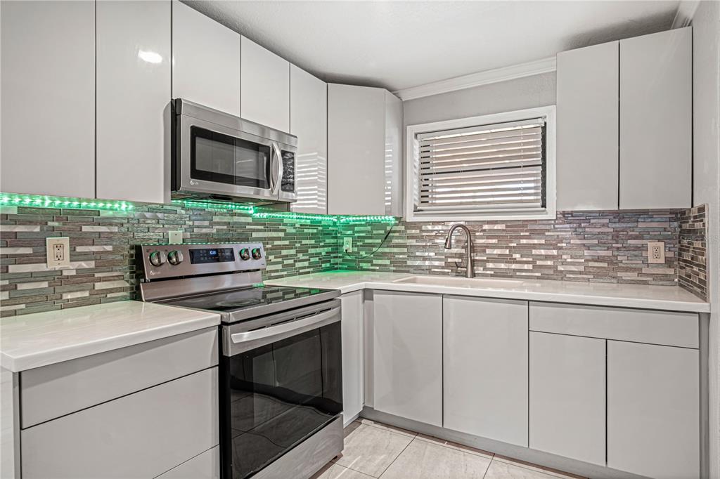 A kitchen features light gray cabinets, stainless steel appliances, and a multicolored glass tile backsplash — 4588 PARKER AVENUE, ROCKLEDGE, FL