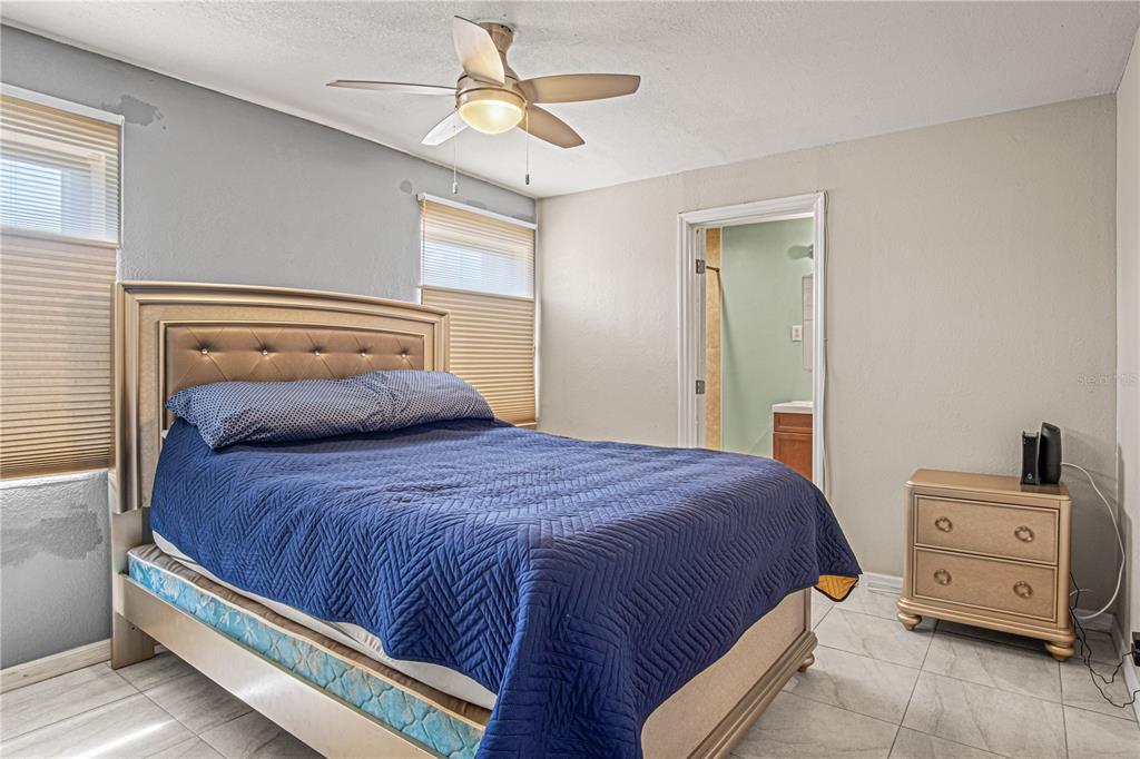 A bedroom with tiled floors, a bed with a blue quilt, and an attached bathroom — 4588 PARKER AVENUE, ROCKLEDGE, FL