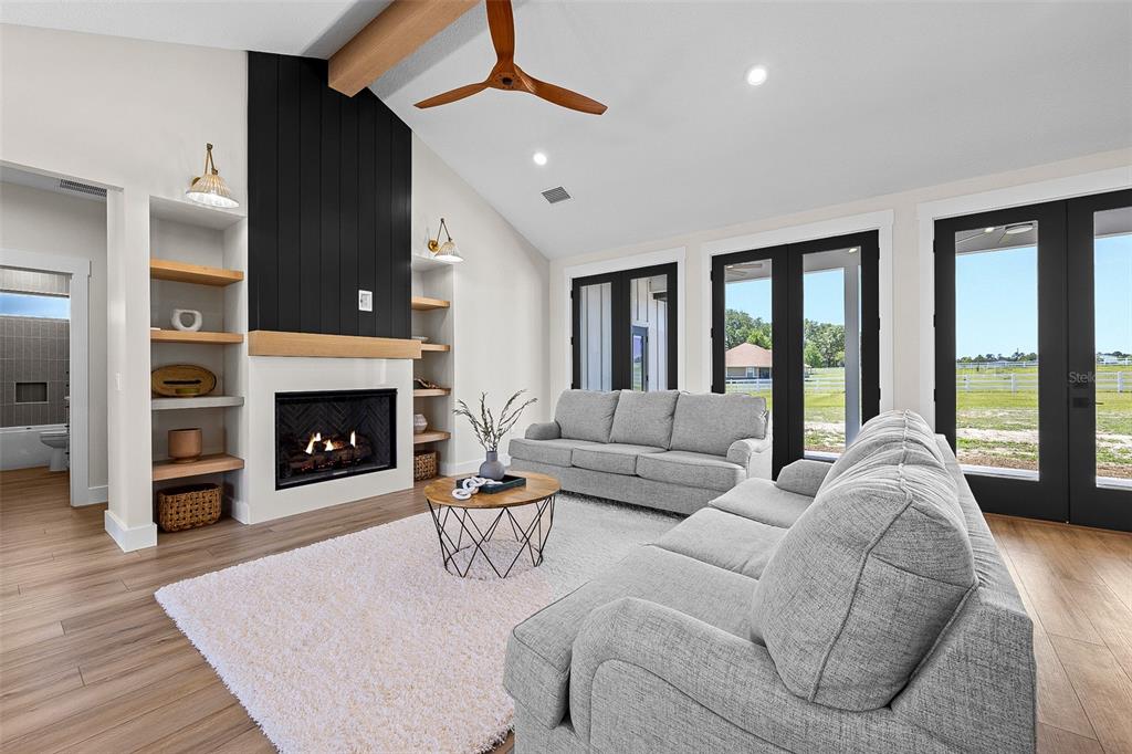 A living room features a black fireplace, wood shelving, grey sofas, and large glass doors — 845 NW COUNTRY LAKE DRIVE, LAKE CITY, FL