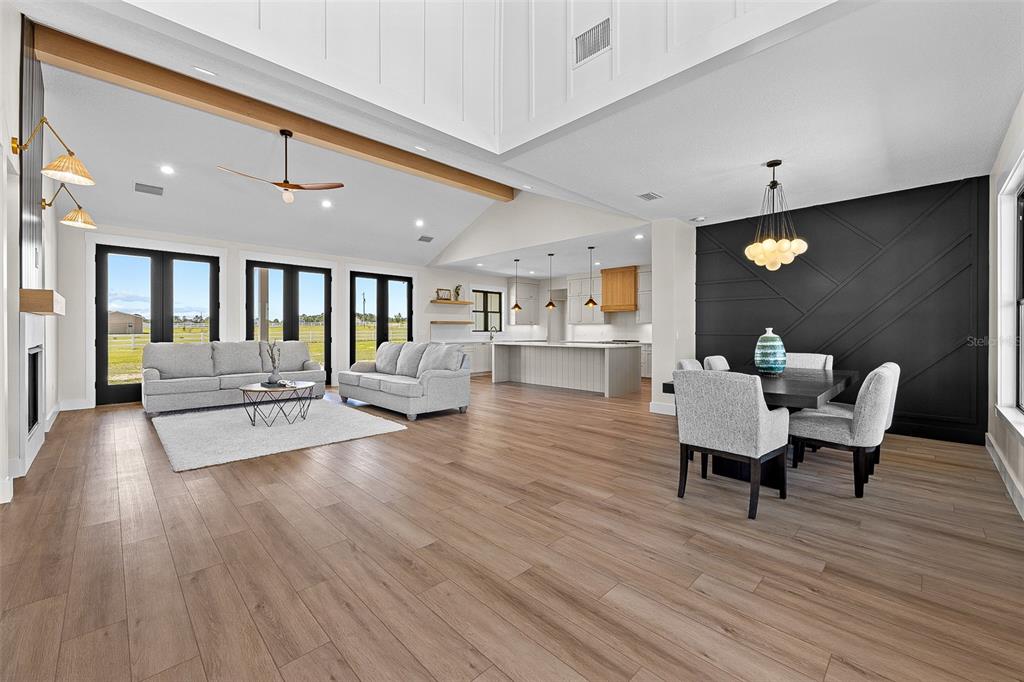 An open-concept living and dining area features wood-look flooring, a vaulted ceiling, and black accents — 845 NW COUNTRY LAKE DRIVE, LAKE CITY, FL