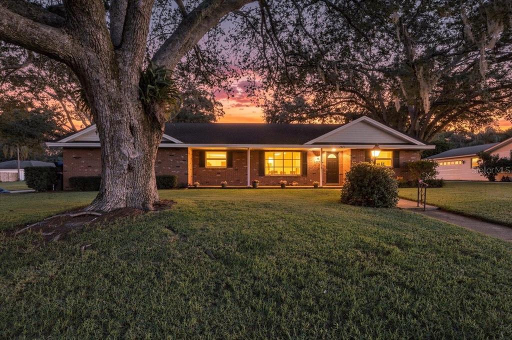 A single-story brick house with a large oak tree in the front yard at sunset — 2021 CHARNES DRIVE, LAKELAND, FL