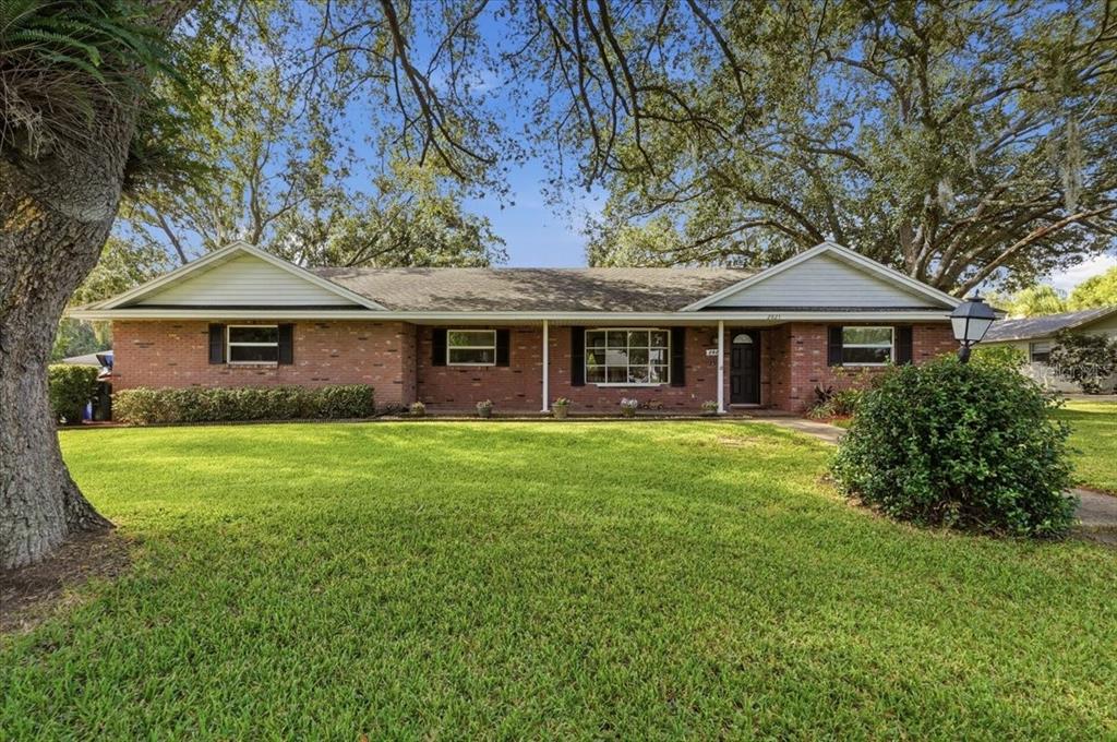 A single-story brick house with a gabled roof, white siding, and a large front lawn — 2021 CHARNES DRIVE, LAKELAND, FL